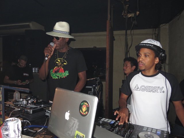 Eek A Mouse in the dj booth holding mic, wearing the T-shirt with portrait graphic by Massa AquaFlow